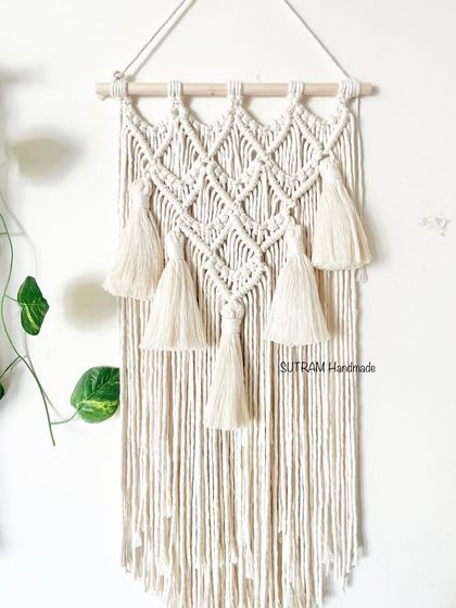 A full view of the 'Jasmine' boho tapestry. It's made with natural off-white cotton and has a beautiful, flowing design with tassels.