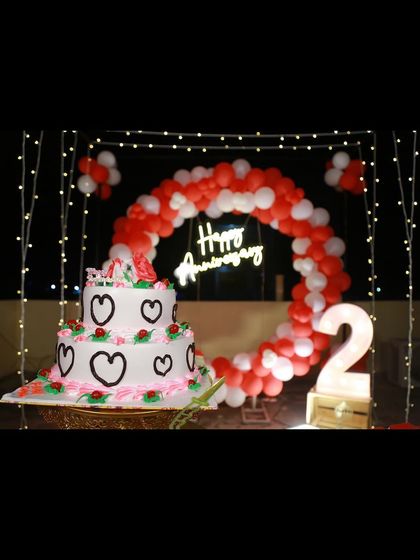 A close-up of the second-anniversary decoration, focusing on the cake placed in front of the red and white balloon backdrop.