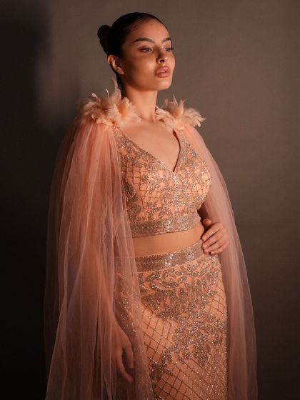 It's all in the details. This stunning straight-fit peach outfit with a sheer cape and feather shoulders is a work of art. It can be rented or customized.