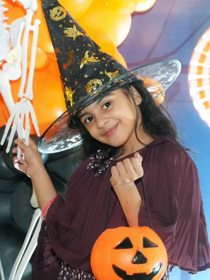 Everyone loves to dress up. This young guest looks adorable in her witch costume, holding a pumpkin basket and ready for some Halloween party fun.