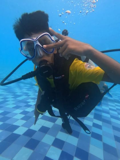 A young scuba trainee flashes a peace sign, showing his comfort and excitement with being underwater.