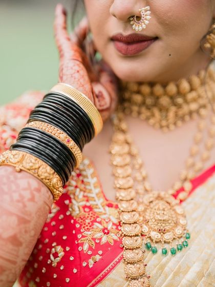 A close up on the details. The traditional black bangles contrast beautifully with the gold jewellery and red saree, while the makeup remains soft with a natural lip color.