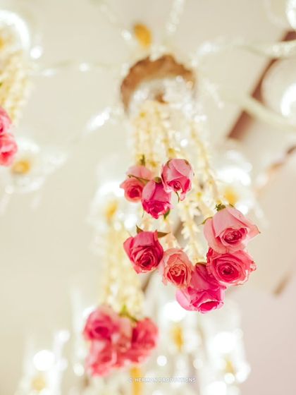 A close-up of a chandelier, with delicate pink rosebuds hanging from strings of pearls. This small, romantic detail adds a bespoke touch to the lighting fixtures.