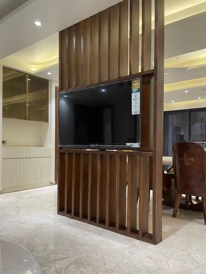 The dual-sided TV panel seen from the living room side. The teakwood jali screen provides a warm, textural element that complements the rest of the interior design.