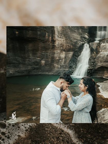A classic romantic gesture as the groom kisses the bride's hand, with a stunning waterfall as their backdrop.