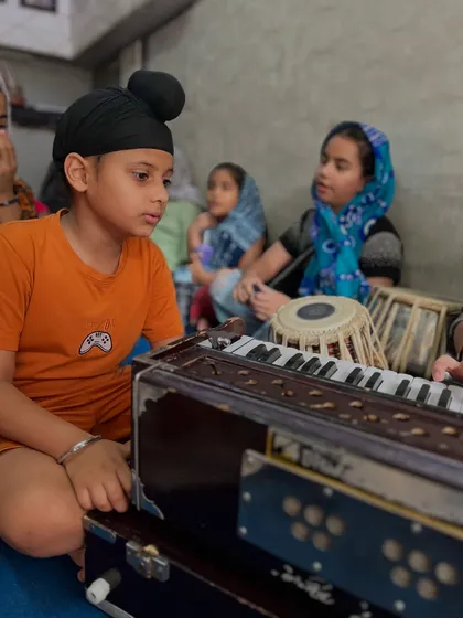 A typical class session where students learn the fundamentals of Indian classical music. Here, a young student intently focuses on his harmonium practice, learning the foundational elements of Raag and Taal.
