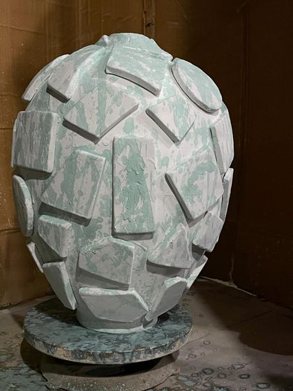 A large, textured Moon Jar after the glaze has been applied but before the final firing. The geometric shapes are built up on the surface, and the green glaze will transform in the kiln.