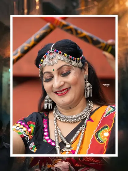 A close-up portrait from a Navratri Garba shoot. The focus is on the dancer's joyful expression and the intricate silver jewelry, with dandiya sticks creating a frame in the background.