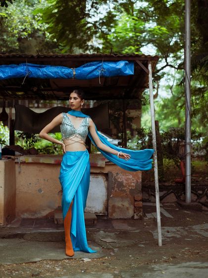 A high-fashion look against a rustic, everyday backdrop. The contrast between the glamorous blue outfit and the street-side stall makes for a striking and memorable image.