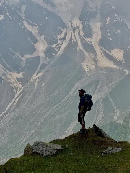 A lone trekker stands on a ridge, gazing at the massive, snow-covered mountains on the Friendship Peak trail.