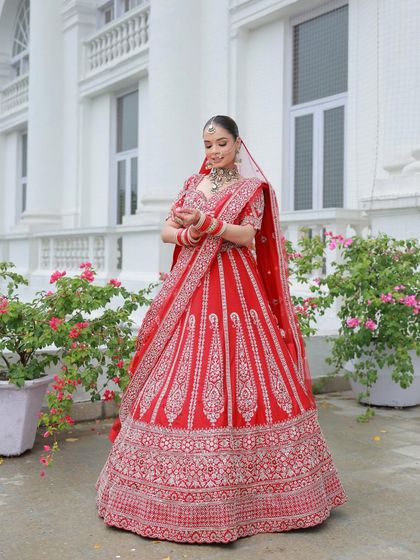 A full-length shot of the bride in her red lehenga, with her hands gracefully together. The outfit exudes tradition and elegance.