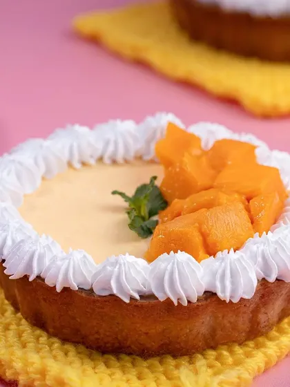 A vibrant Mango Shrikhand Tart on a yellow coaster against a pink background. The playful use of color makes this dessert photo pop.