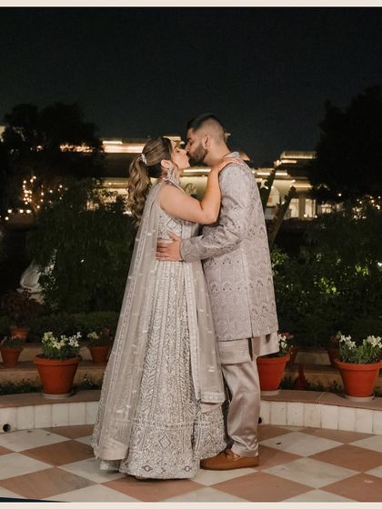 The couple shares a romantic kiss at their outdoor engagement party. The nighttime setting with twinkling lights creates a magical and intimate atmosphere.