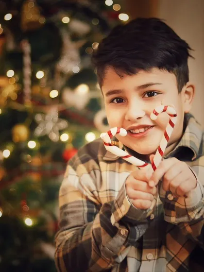 The pure joy of Christmas, captured in a smile and a handful of candy canes. The twinkling lights of the tree create a magical bokeh effect in the background.