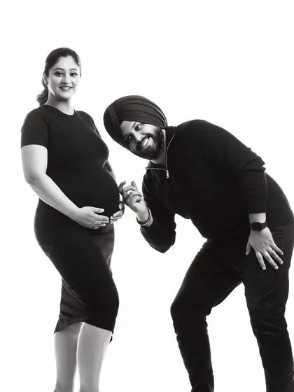 A fun and playful black and white portrait. The dad-to-be leans in to 'listen' to the baby bump, creating a lighthearted and joyful image of the couple.