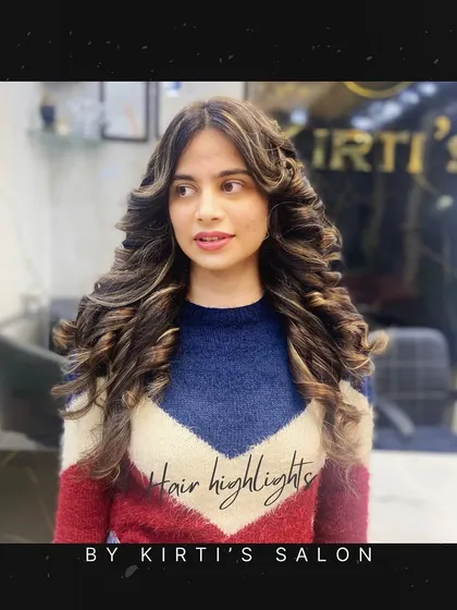 A portrait of the client with the curly, highlighted hair. She looks stylish and confident in her cozy sweater and gorgeous hair.