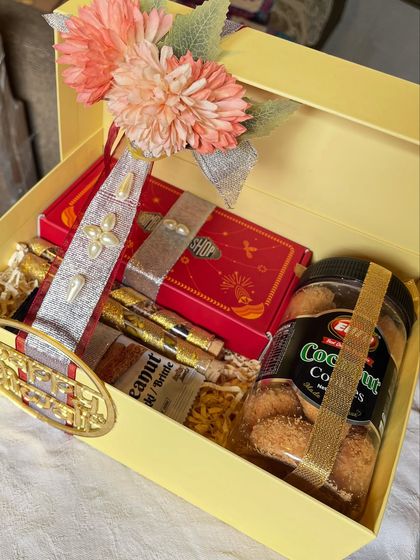 A beautiful Diwali hamper in a yellow box, filled with coconut cookies, dry fruits, and other sweet goodies. The pearl and floral decorations add an elegant touch.