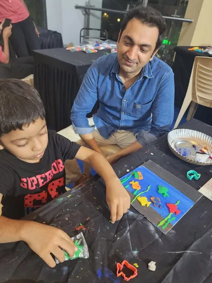 A father watches proudly as his son creates a colorful underwater scene with clay. My family bond workshops are designed to create these moments of shared creativity and connection.