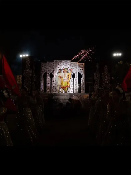 An aisle of light for the royal couple. Dancers with red flags line the path, creating a dramatic and regal walkway leading to the varmala stage.