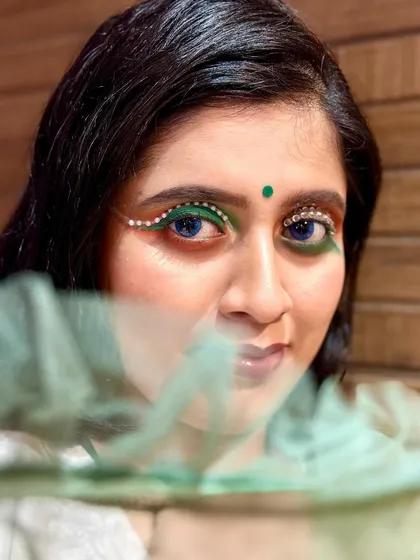 A creative makeup look for Independence Day, using rhinestones to create a winged liner effect. The green bindi and blue contact lenses add to the thematic concept.