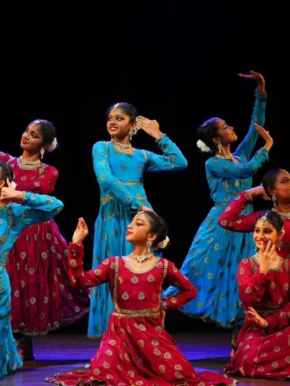 My talented students from the Sāttvatī School of Dance in a dynamic pose during our "ARAMBH" performance, dressed in vibrant red and blue costumes.