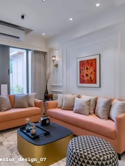 A warm and inviting living room with peach-colored sofas and classic wall molding. The gold and black coffee table adds a modern touch to the otherwise traditional space.