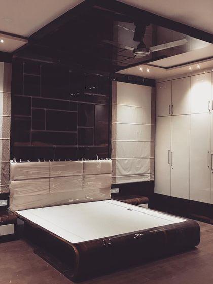 The finished bedroom, with a high-gloss black ceiling panel reflecting the light. The combination of dark wood, white wardrobes, and soft lighting creates a dramatic and luxurious ambiance.