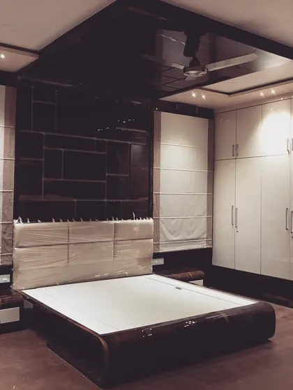 The finished bedroom, with a high-gloss black ceiling panel reflecting the light. The combination of dark wood, white wardrobes, and soft lighting creates a dramatic and luxurious ambiance.