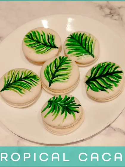 Our Tropical Cacao Macarons. These feature a rich chocolate filling and are decorated with a hand-painted tropical leaf, combining classic flavor with an artistic touch.