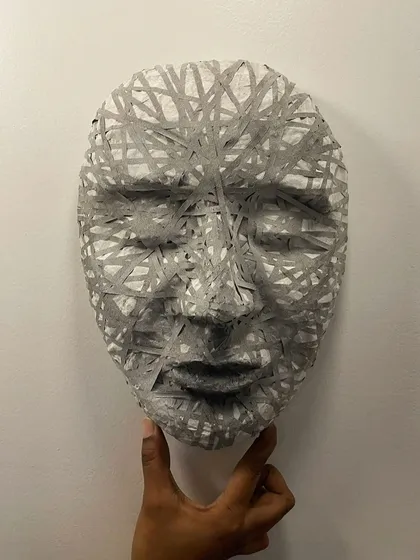 A pensive mask created with paper-mâché and upcycled cassette tape. The interwoven tape creates a complex texture, representing the layers of thought and emotion we all carry.