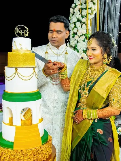 A slightly different angle of the couple cutting their cake, showing the beautiful details of the bride's saree and the cake's design.