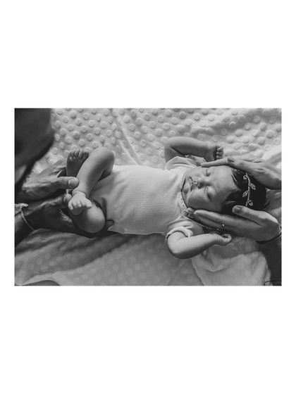 A black and white overhead shot of a newborn being cradled by her parents' hands. This artistic photo highlights how small and protected the baby is.
