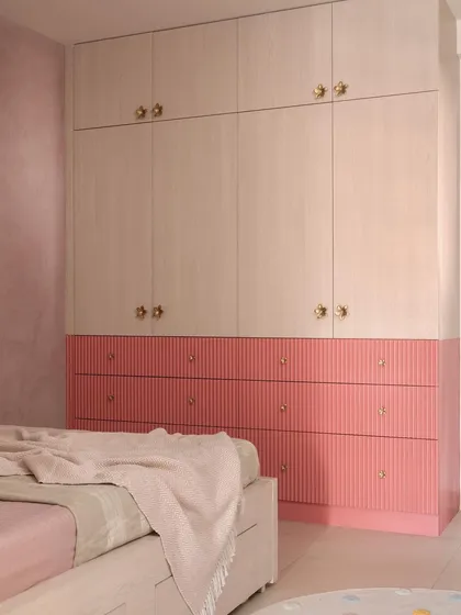A closer look at a custom wardrobe I designed for a child's room, featuring a playful yet chic two-tone design. The fluted pink drawers add texture and color, while the light wood-finish upper cabinets with delicate gold knobs provide ample, stylish storage.