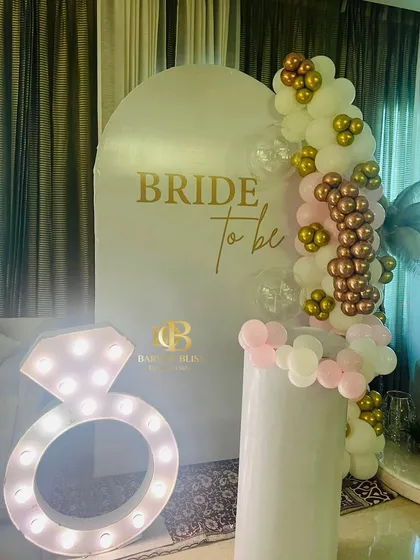 A glamorous 'Bride to be' photo corner. This setup includes a personalized backdrop, a balloon arrangement, and a large light-up marquee prop in the shape of a diamond ring.