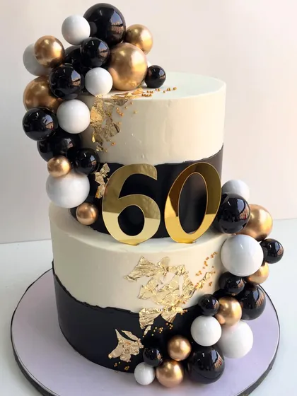 A closer look at the black, white, and gold 60th celebration cake, focusing on the bold number topper and the shimmering gold leaf details.