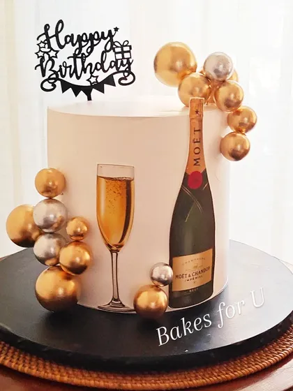 A celebratory cake with a Moët & Chandon theme. The simple white cake is decorated with an edible image of the champagne bottle and glass, surrounded by gold and silver spheres.