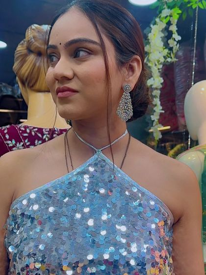 A close-up of a model trying on a sequined ice-blue halter top, part of a lehenga set. The matching diamond chandelier earrings complete this chic look.