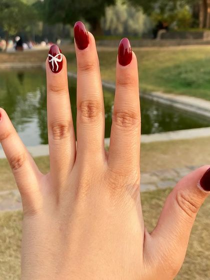 Holiday cheer at your fingertips. This client is showcasing her festive Christmas nails, featuring a deep red polish and a delicate, hand-painted bow accent nail.