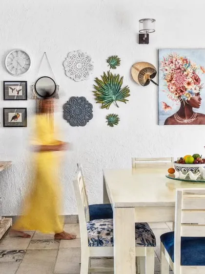 A Mediterranean-inspired living and dining area with white-washed walls and pops of royal blue. The gallery wall, filled with travel souvenirs and art, creates a personal and vibrant atmosphere.