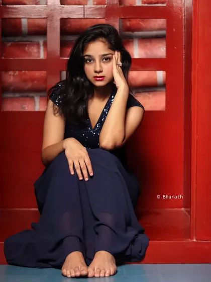 A striking portrait of a model in a navy blue sequined gown, set against a bold red brick background. The color contrast is dramatic and effective.