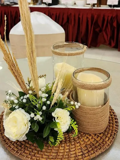 A close-up of a bohemian-style table centerpiece. I used a woven rattan base, candles in glass jars, and a simple arrangement of white flowers and dried wheat stalks.