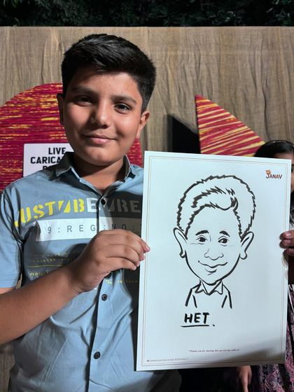 A young boy proudly holding his finished caricature at a party with a "Live Caricature Booth" in the background.