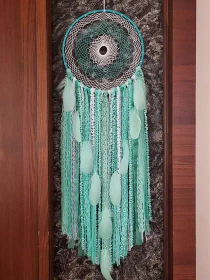 Infuse your space with serenity and charm. This simple yet elegant green dreamcatcher with soft feathers weaves its own special kind of magic.