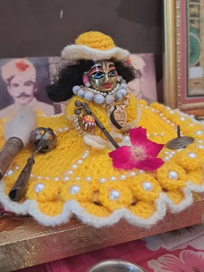 A simple yet elegant yellow woolen poshak, perfect for daily wear. This dress is adorned with white pearls along the scalloped edge and comes with a matching cap to keep your Laddu Gopal looking charming and feeling warm.