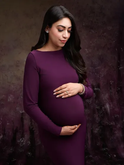 This elegant portrait in a rich plum-colored gown highlights a quiet moment of reflection. The textured, dark purple backdrop complements the dress and adds a touch of artistic sophistication.