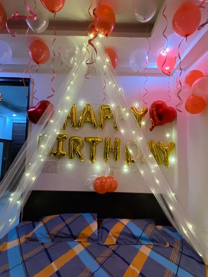 This birthday setup features a beautiful cabana made of sheer fabric and fairy lights over the bed. It creates a cozy and magical focal point in the room, complemented by 'Happy Birthday' foil balloons.
