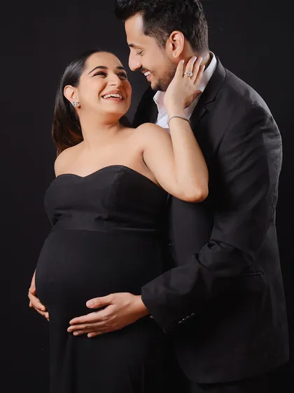 An intimate moment between an expecting couple, both dressed in classic black. This studio portrait focuses on their happy expressions and the shared excitement of their journey.