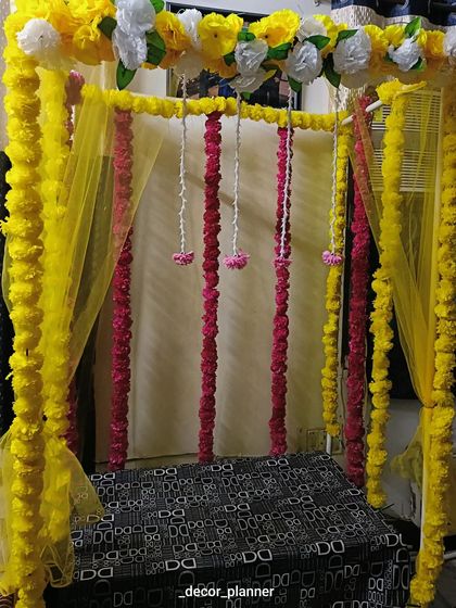 A simple yet beautiful Ganpati setup with a canopy of yellow marigold garlands and sheer yellow drapes. The hanging strings of pink flowers add a lovely pop of color.