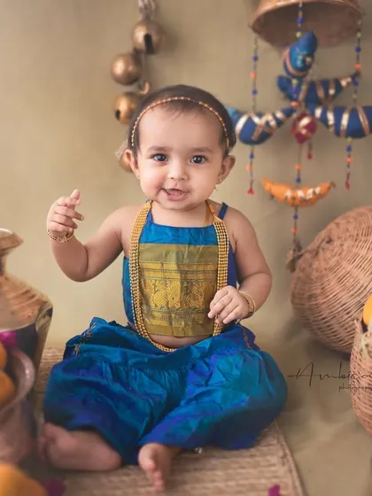 This little one's sweet expression and gesture are just priceless. The setup is filled with authentic details like brass pots and woven baskets.