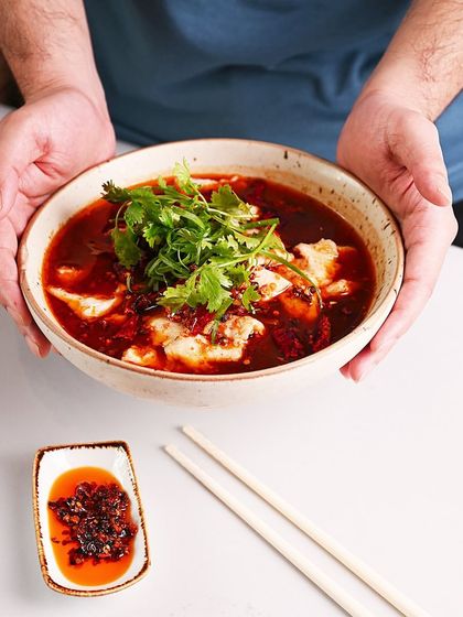 A vibrant and spicy fish dish, served in a rustic bowl. The bright red chili oil broth is topped with a generous amount of fresh cilantro, promising a bold flavor experience.